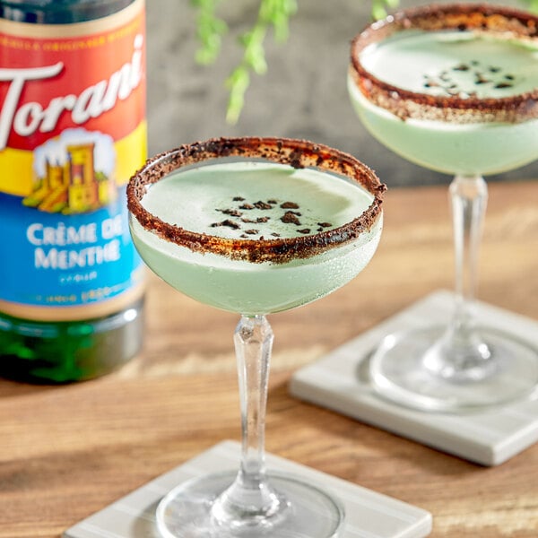 Two martini glasses filled with green Torani Creme de Menthe drinks on a table in a cocktail bar.