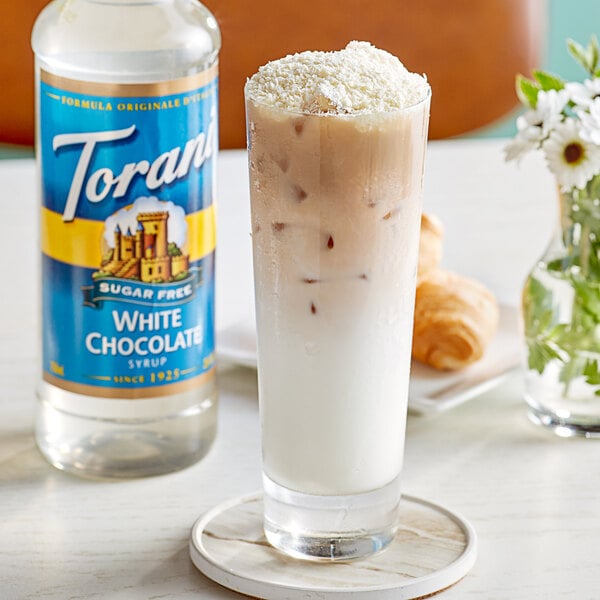 A glass of milkshake with a Torani Sugar-Free White Chocolate Flavoring Syrup bottle.