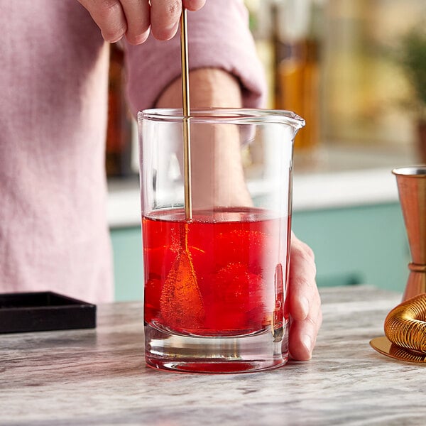 A person mixing a red cocktail in an Acopa cocktail stirring glass.