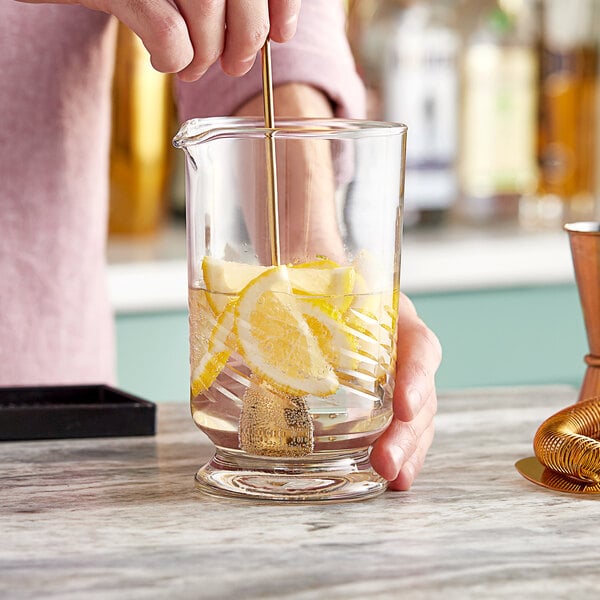 A person mixing a drink in an Acopa footed cocktail stirring glass with a spoon.