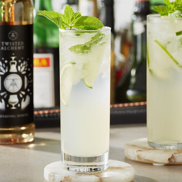 A glass of Twisted Alchemy simple syrup with lime and mint on a coaster.