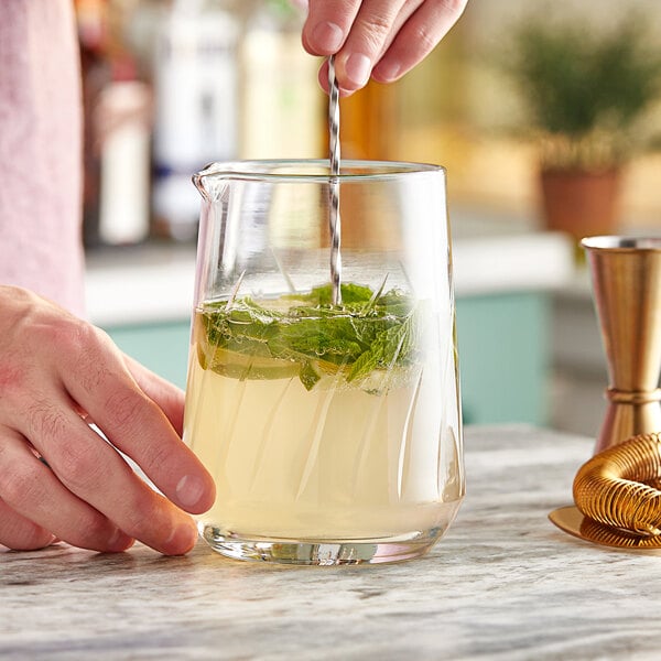 A hand using an Acopa striped mixing glass to mix a cocktail.