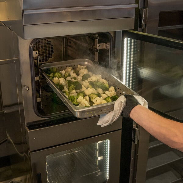 A person holding a tray of broccoli and cauliflower in a Henny Penny electric combi oven.