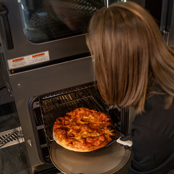 A woman using a Henny Penny FlexFusion electric combi oven to cook a pizza.