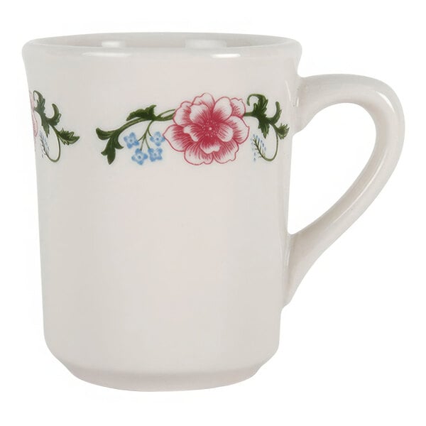 A white Tuxton china mug with a floral design of pink flowers and green leaves.