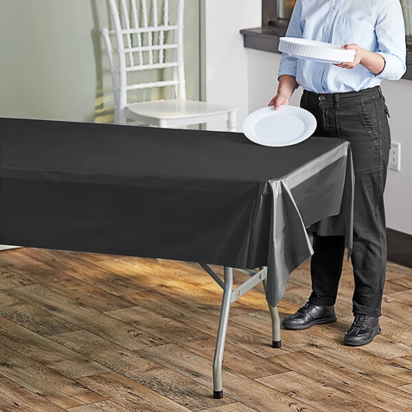 A woman standing next to a black plastic table covered with a white plate.