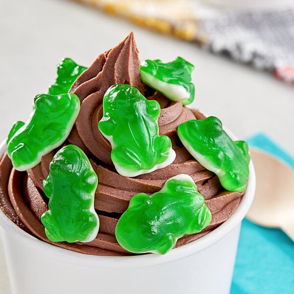 A cup of chocolate ice cream with Vidal green frog gummies on top.