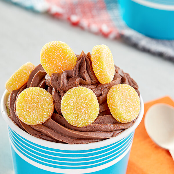 A cup of chocolate ice cream with Vidal Sour Gummy pineapple and orange bites on top.
