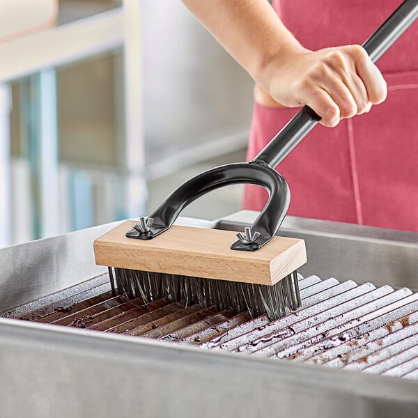 A person using a Choice stainless steel bristle grill brush to clean a grill.
