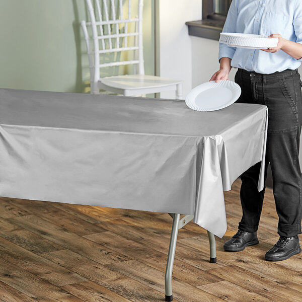A woman holding a white paper plate in front of a metallic silver plastic table cover on a table.