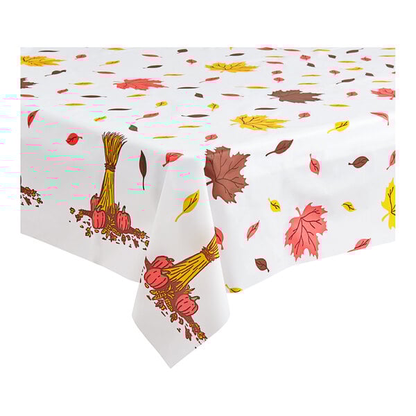 A white tablecloth with fall leaves and pumpkins on it.