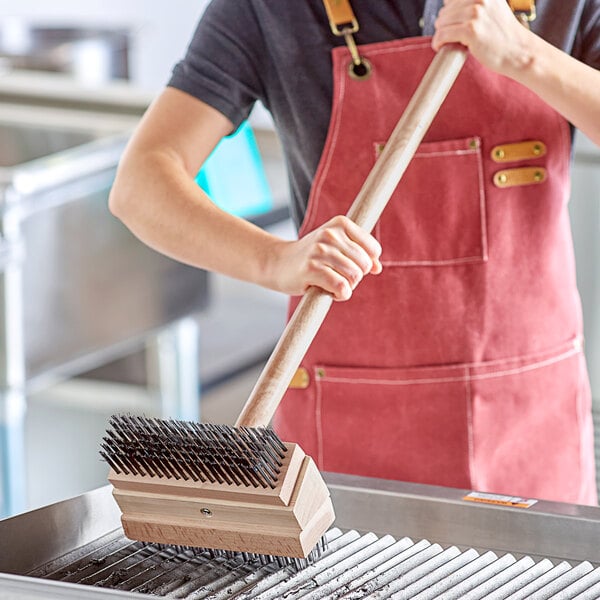 A person using a Choice Double Head Grill Brush with Coarse Scraping and Medium Bristles to clean a grill.