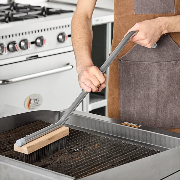 A person using a Choice steel bristle grill brush to clean a grill.