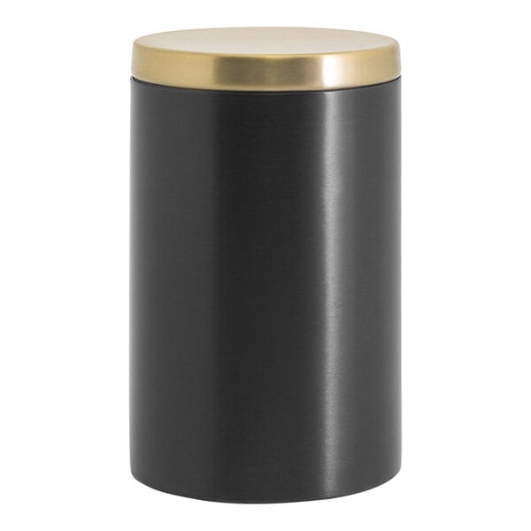 A black stainless steel canister with a matte brass lid on a white table.