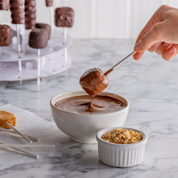A person using a Paper Lollipop Stick to dip a marshmallow in chocolate.