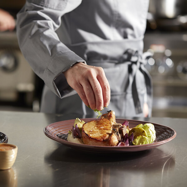A person's hand putting a piece of food in a Libbey mauve terracotta coupe bowl.