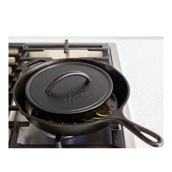 A Lodge cast iron grill press on a black skillet on a stove.