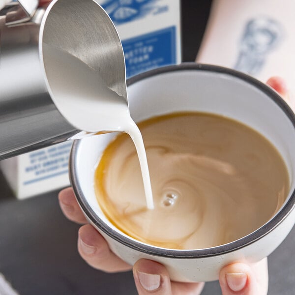 A person pouring Almond Breeze Barista Collection Unsweetened Almond Milk into a cup of coffee.
