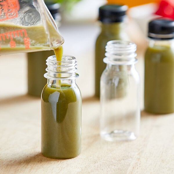 A person pouring a green liquid into a 2 oz. clear PET bottle on a counter.