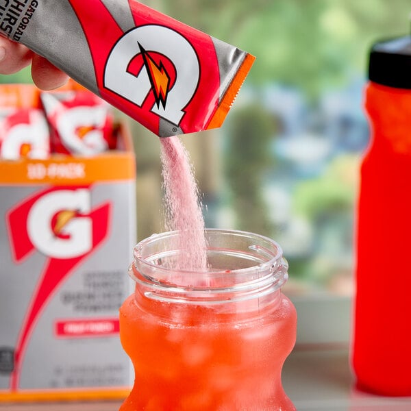 A hand pouring Gatorade Fruit Punch powder into a glass.