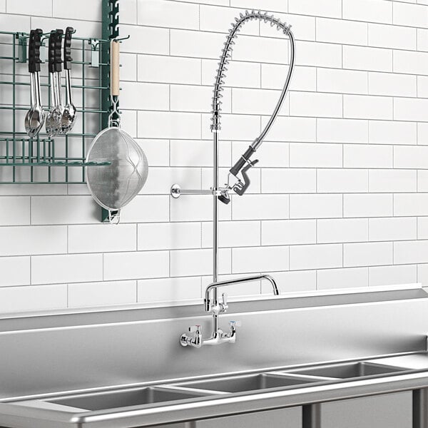 A wall-mounted pre-rinse faucet and add-on faucet above a sink with utensils.