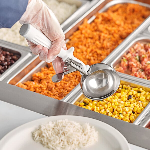 A person holding a Fourté white metal scoop over a tray of food.