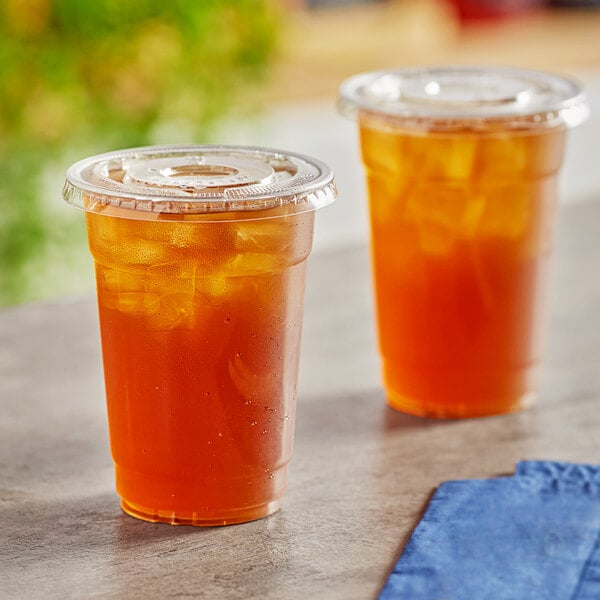 Two Choice clear plastic cups of iced tea on a table.