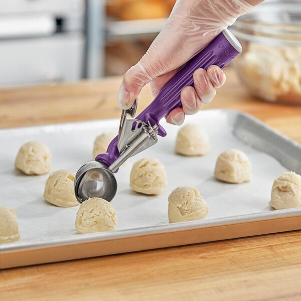 A hand holding a Fourt&#233; purple thumb press scoop over small round objects.