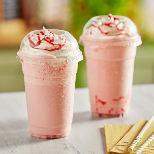 Two Choice clear plastic cups of pink drinks with whipped cream and straws.