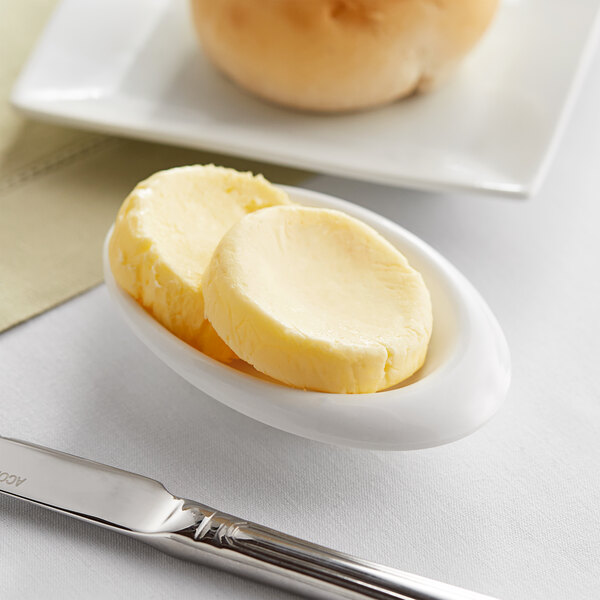 A spoon with Echire unsalted butter next to a knife on a white plate with a bread roll.