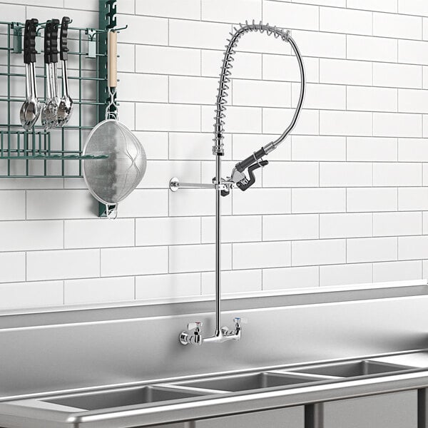 A wall-mounted pre-rinse faucet over a kitchen sink with utensils on a rack.