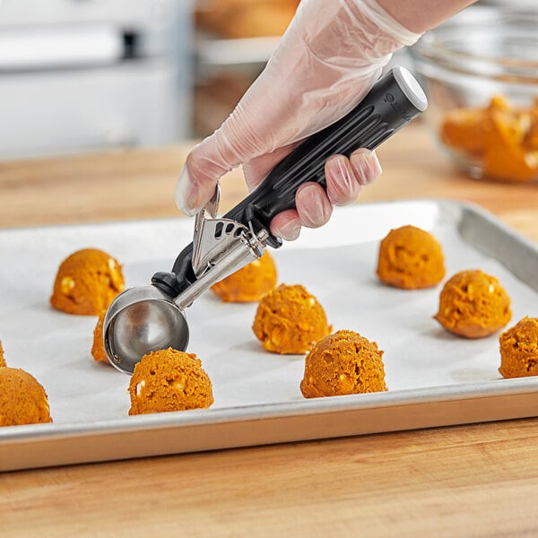 A hand holding a black Fourt&#233; thumb press scoop over round cookies.