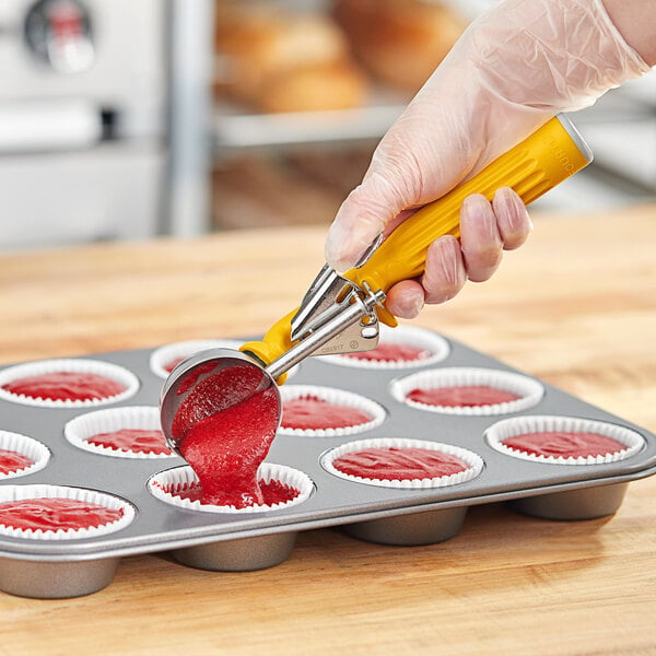 A hand using a Fourté yellow thumb press disher with a white bowl over a cupcake tin.