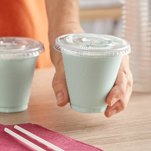 A person holding a Choice clear plastic cup with a straw.