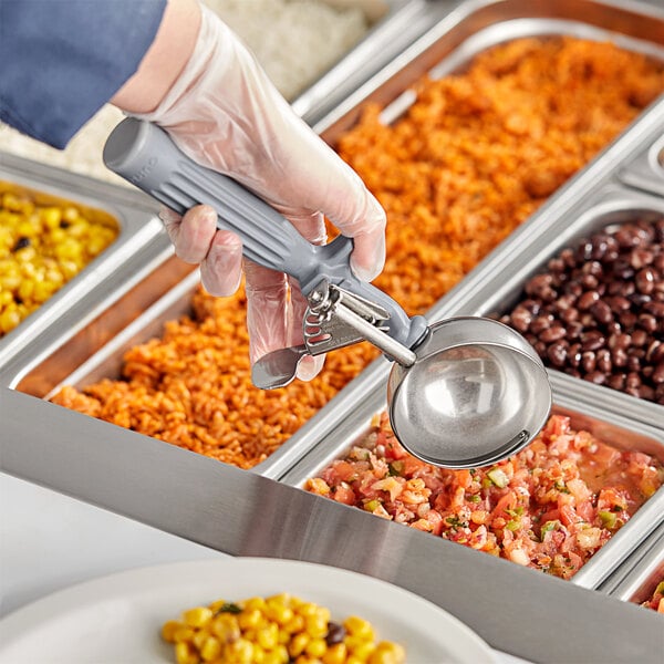 A hand holding a Fourté gray thumb press scooper over a tray of food.