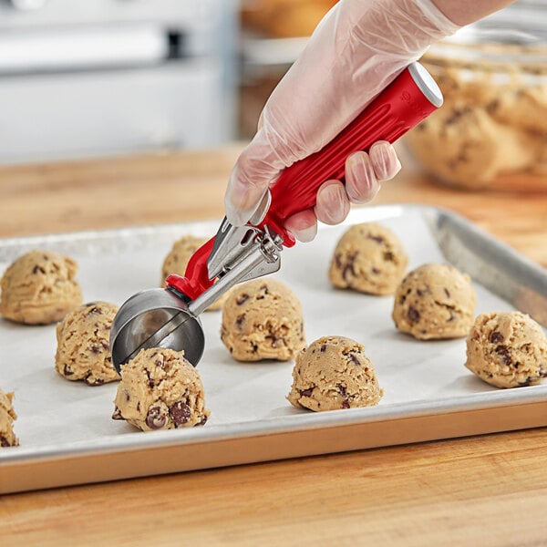 A hand using a Fourté red thumb press disher to scoop cookie dough.