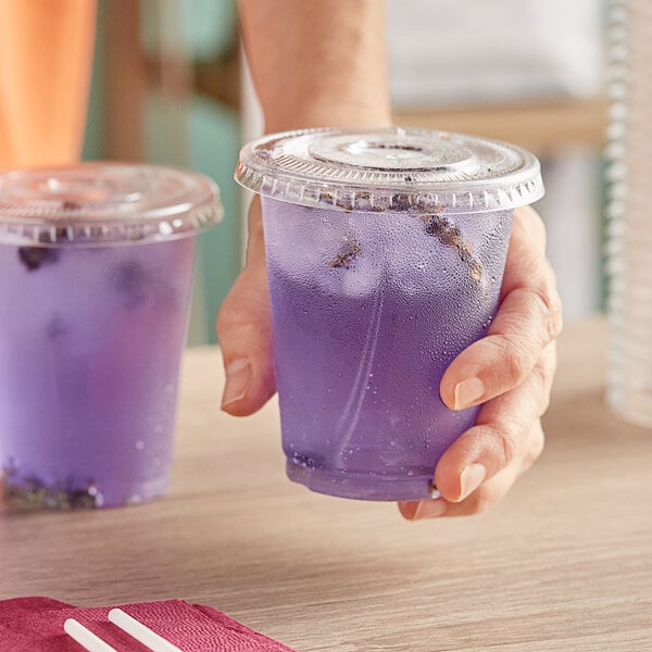 A person holding a Choice clear plastic cup of purple liquid with a straw.