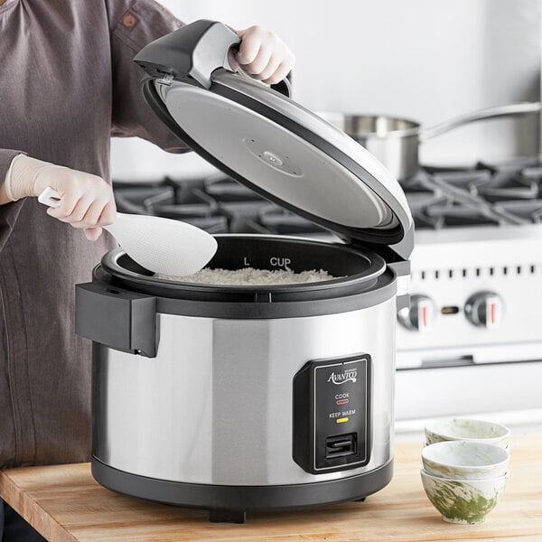 A woman using an Avantco commercial rice cooker to cook rice.