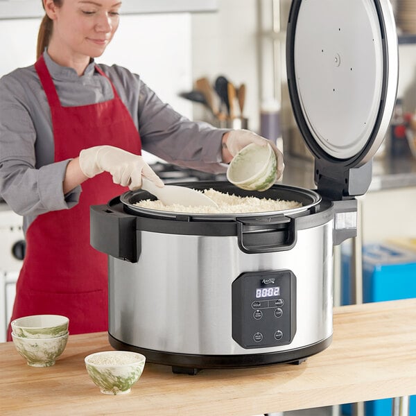 A woman in a red apron using an Avantco commercial rice cooker to cook rice.