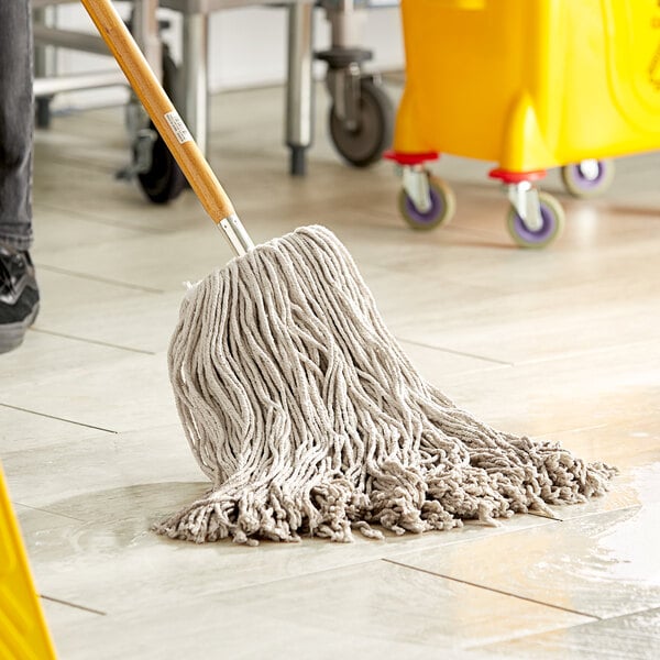 A person mops the floor in a hospital cafeteria with a Lavex natural cotton mop head on a handle.