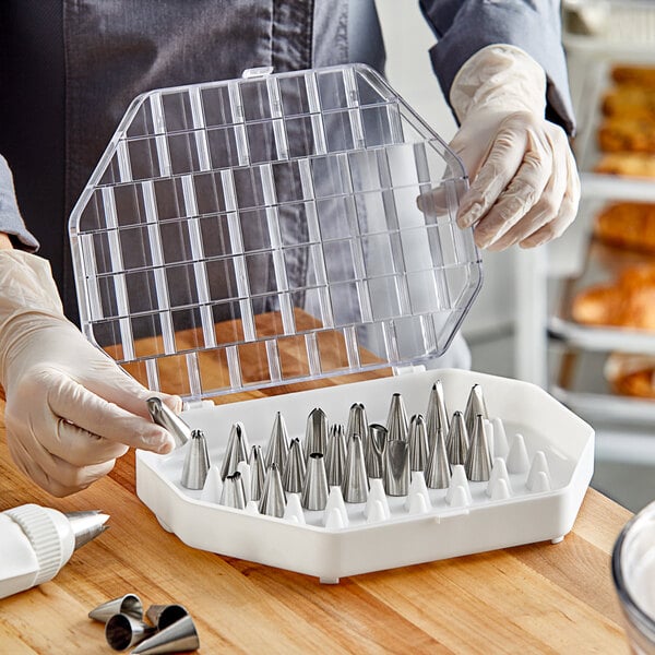 A person in gloves holding a plastic container with Ateco pastry tip compartments.