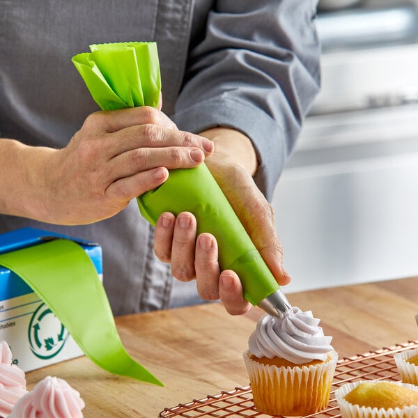 A person decorating a cupcake with a green Ateco pastry bag.