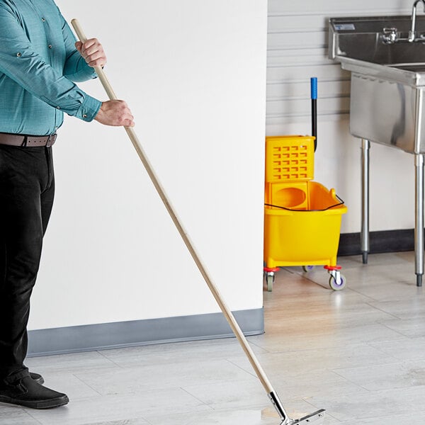 A man using a Lavex wooden broom/squeegee handle to clean a sink.