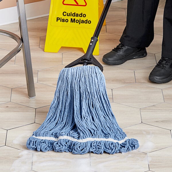 A person mops the floor with a blue Lavex cotton mop head.