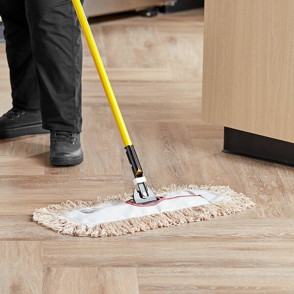 A person using a Lavex white cotton looped end dry dust mop to clean the floor.
