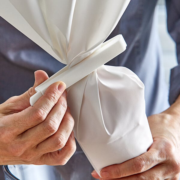 A person using an Ateco white pastry decorating bag clip to close a white pastry bag.