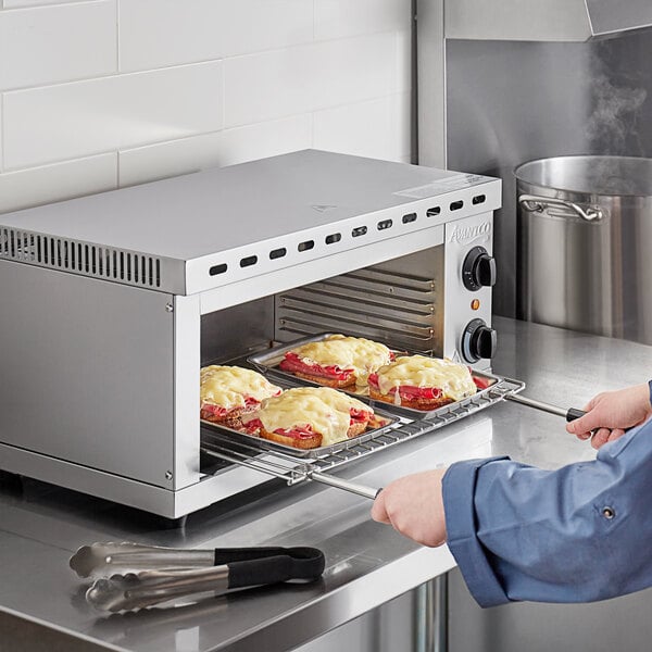 A person using a spatula to cook food in an Avantco electric countertop cheese melter.