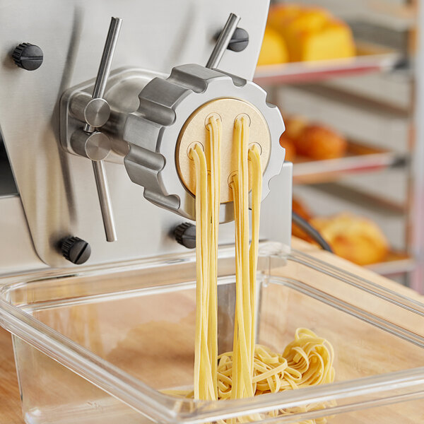 A yellow Estella pasta machine with #32 tagliolini noodles coming out of it.