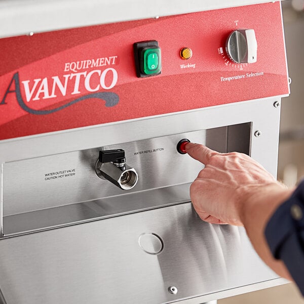 A person using a hand to press a button on an Avantco electric countertop pasta cooker.