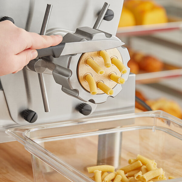 A hand using a black and yellow Estella rigatoni pasta die to make rigatoni pasta.